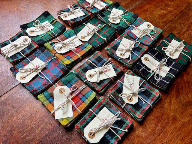 Assorted packaged sets of Tartan Coasters on a wooden table