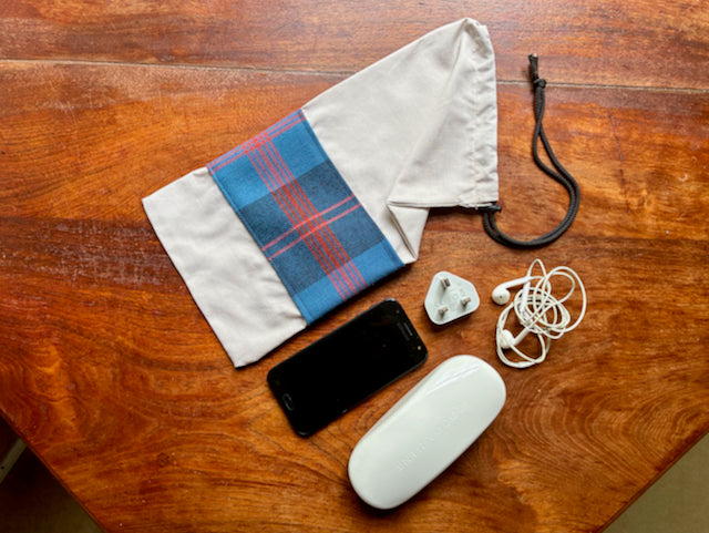 Blue Tartan banded Tartan Drawstring Bag with Phone, mouse, and earbuds on a wooden table