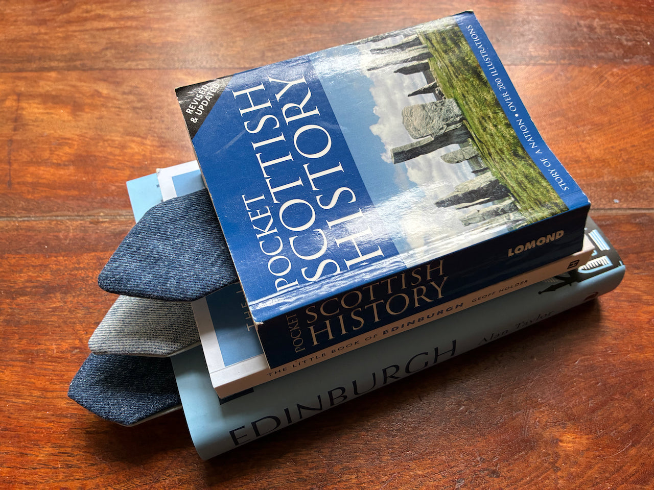 Three books in a pile each with a Deni Bookmark holding the reader's place on a wooden surface