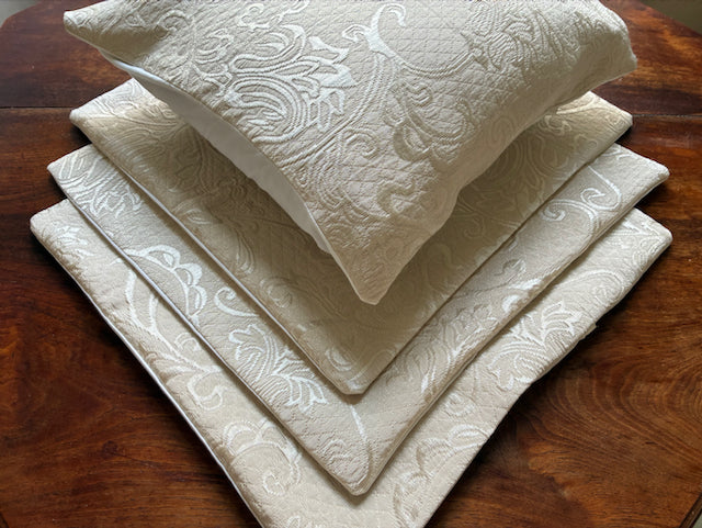 Four Ivory Brocade Cushion covers on a wooden surface