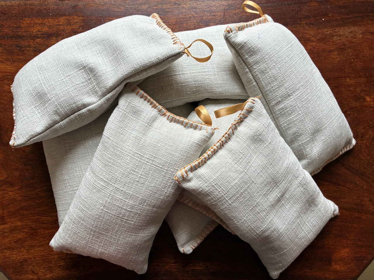Collection of Neutral Linen Wheat Bags  with gold ribbons on a wooden surface
