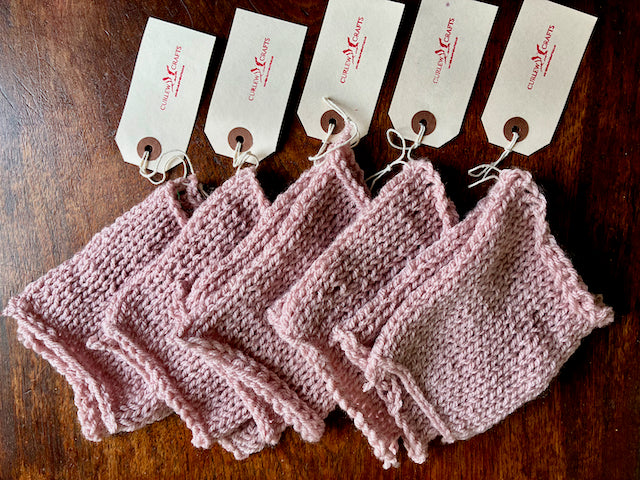 Five Pastel Pink Sets of Knitted Cleaning Cloths on a wooden surface 