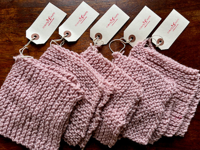 Five Pastel Pink Sets of Knitted Cleaning Cloths on a wooden surface 