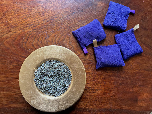 Four Small Purple Lavender Sachets with Satin ribbons by a saucer of Dried Lavender