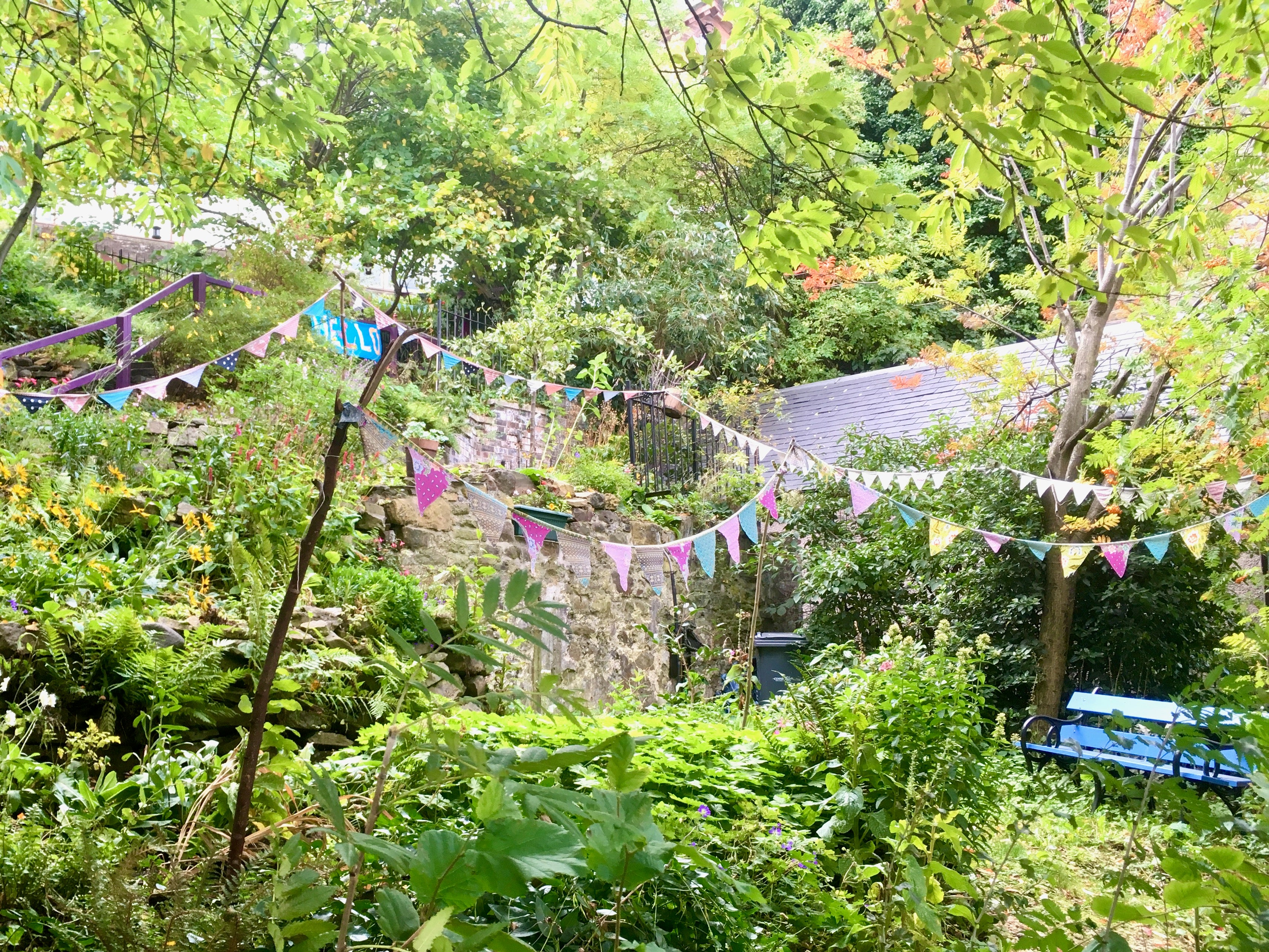 Garden with stone wall and colourful bunting, surrounded by trees and foliage.