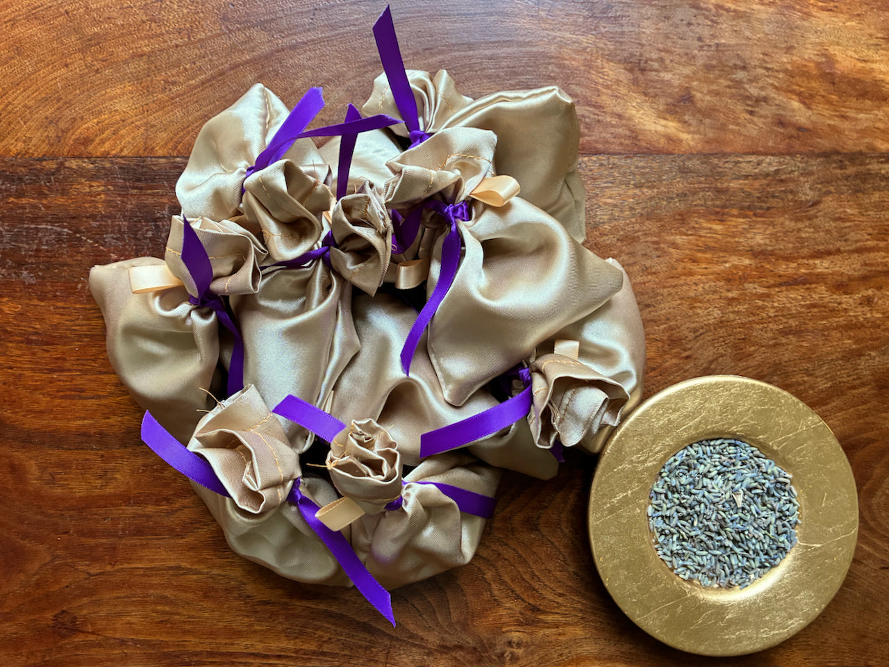 Pile of Gold Silk Lavender Bags with Purple Satin Ribbons next to a Gold bowl of Lavender buds