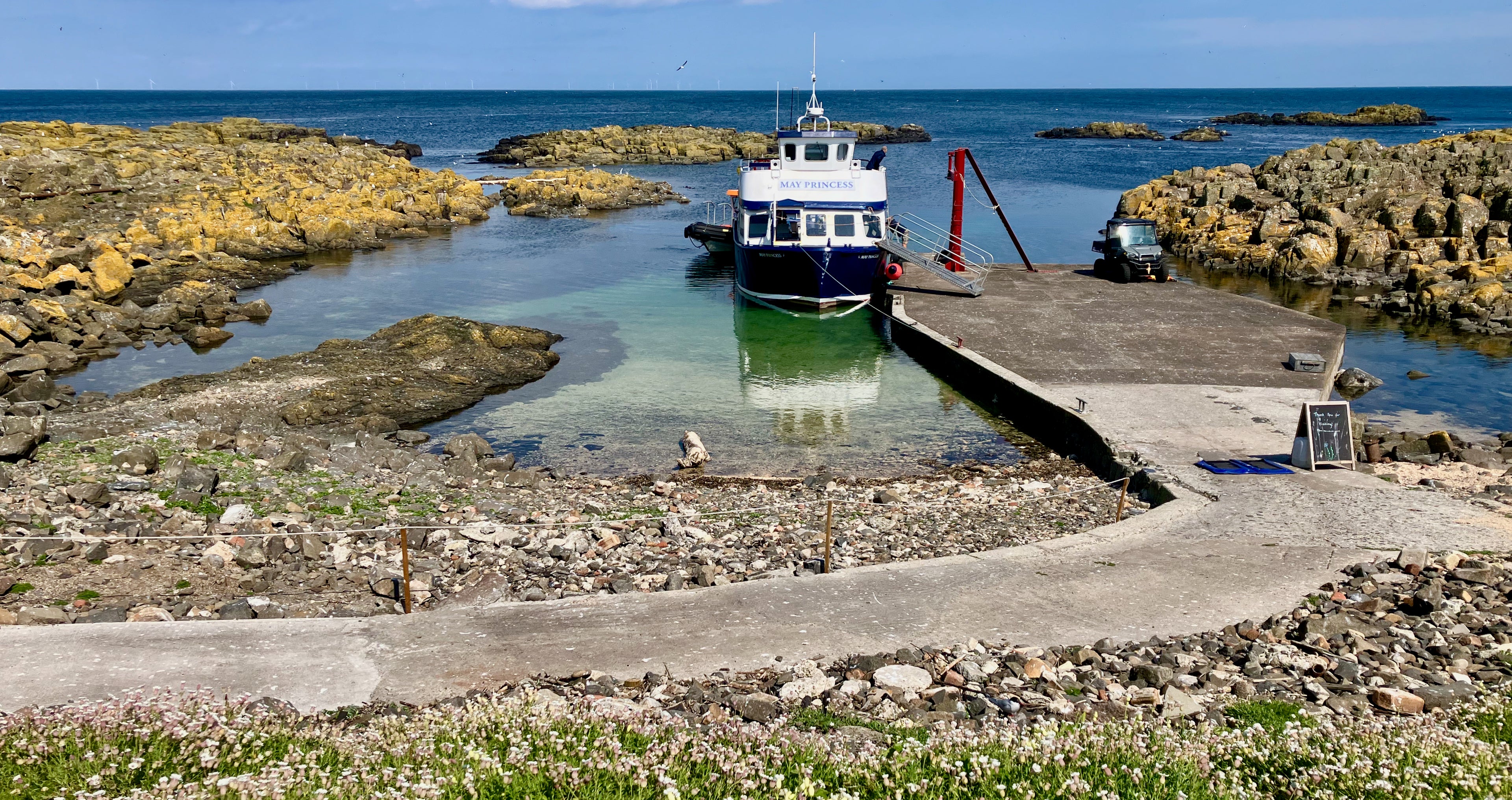 Boat docked at a small pier surrounded by rocky landscape and clear water.