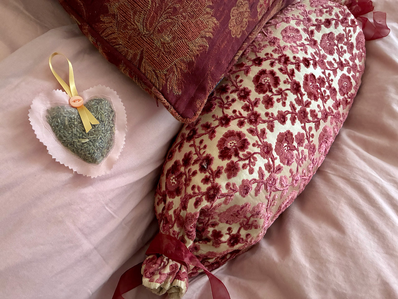 Pink Heart shaped Lavender Pillow Sachet on a pink pillow with decorative cushions.