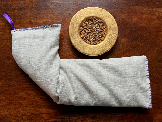Lavender Wheat Bag with Purple ribbon and embroidered edging by a bowl of Wheatgrain