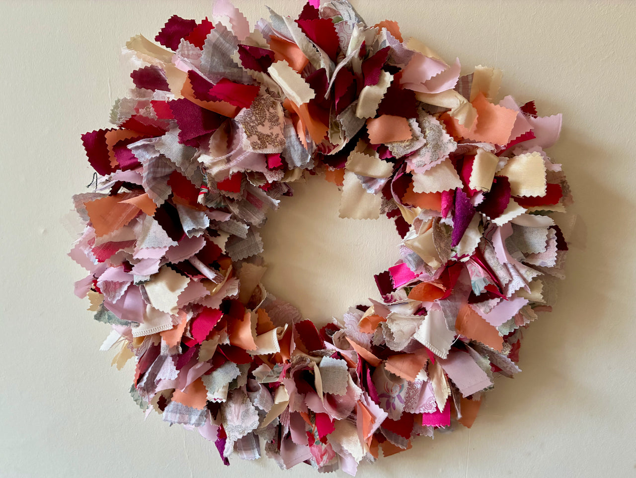 Seasonal circular Fabric Wreath with romantic Reds, Pinks, Creams and Reds on a Cream wall