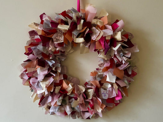 Multicolored fabric wreath in reds and pinks on a cream wall