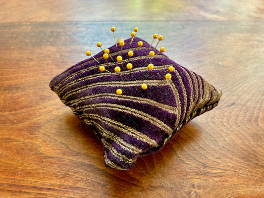 Purple and gold Art Deco Chenille pin cushion with pins on a wooden surface