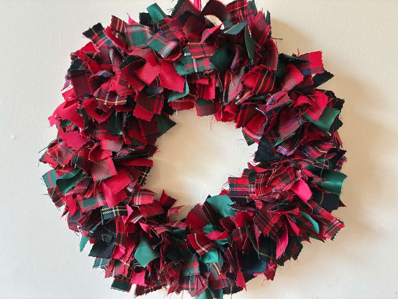 Seasonal circular Winter Wreath with Red, Green, and Gold Colours on a cream wall