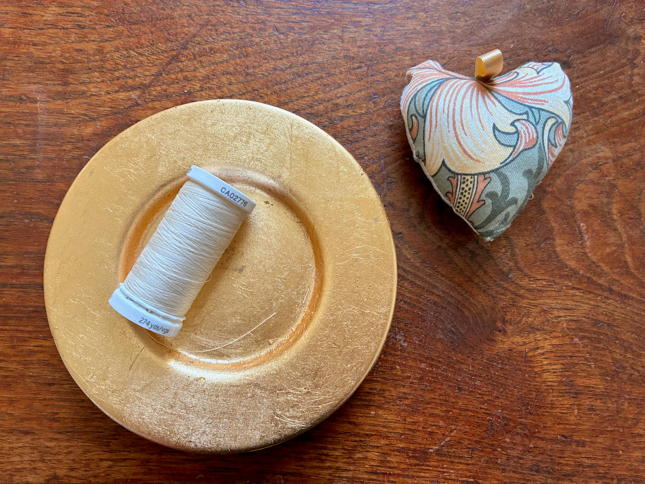 One Small William Morris Heart Pincushion by a saucer with thread in  it