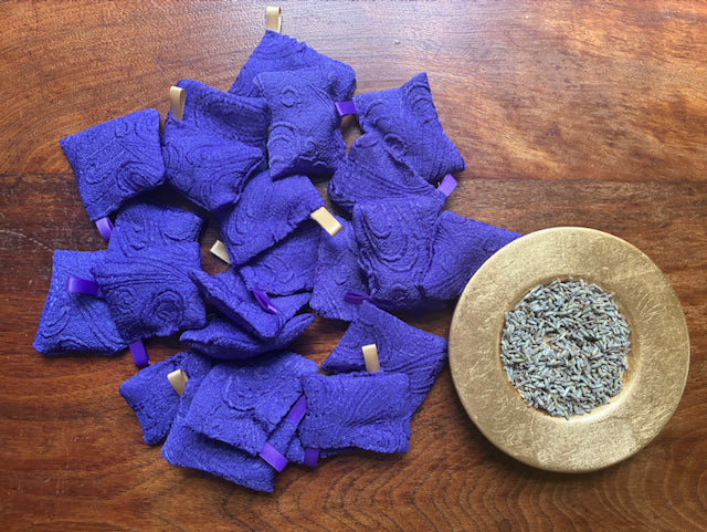 Small Purple Lavender Sachets by a Gold saucer of Lavender on a wooden table
