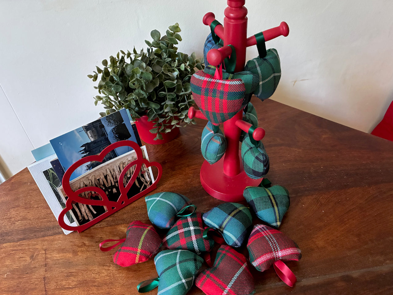 Assorted small decorative Tartan Hearts by a plant and a letter rack on a wooden surface