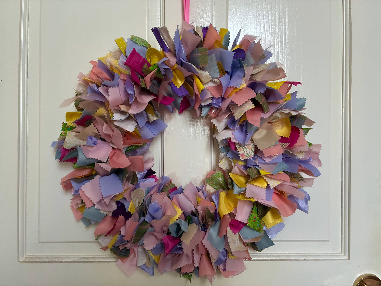 Sustainable circular wreath in Springtime yellows, pinks, lilacs and greens hanging on a door