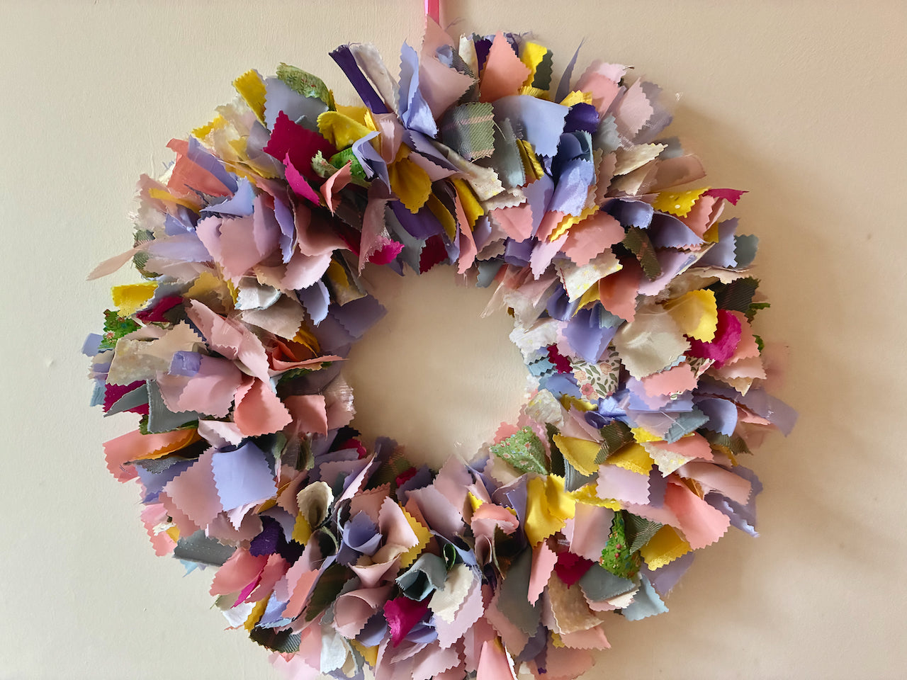 Seasonal circular fabric Wreath in Springtime Yellows, Pinks, Lilacs, Greens and Peaches on a Cream wall
