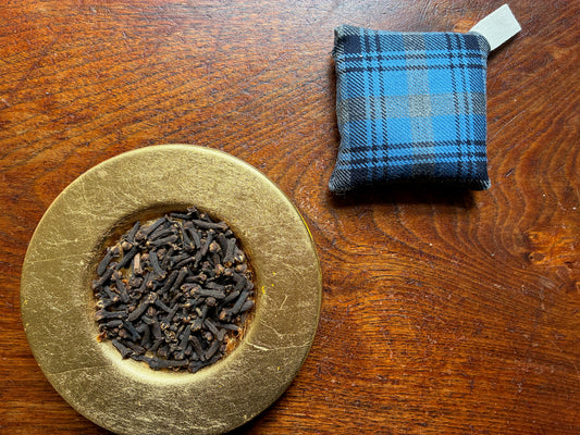 One Square Tartan Clove Sachet by a saucer of Whole Cloves on a wooden surface