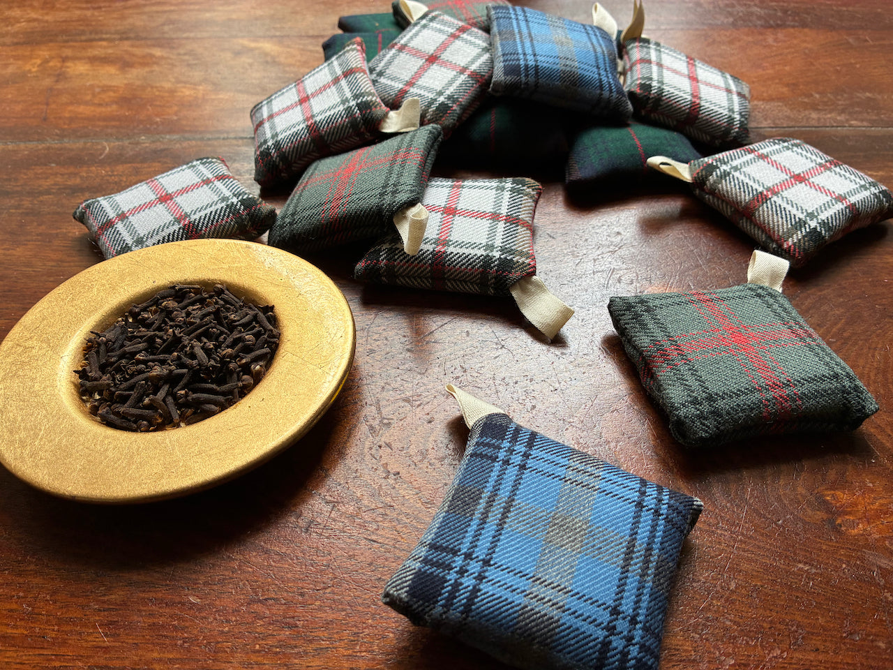 Assorted Square Tartan Clove Sachets by a saucer of Whole Cloves on a weooden surface