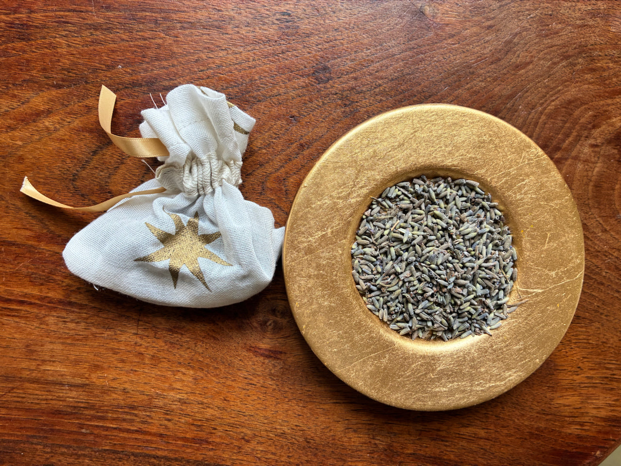 Small white Lavender Bag with Gold stars by Curlew Crafts beside a Gold dish of dried Lavender buds