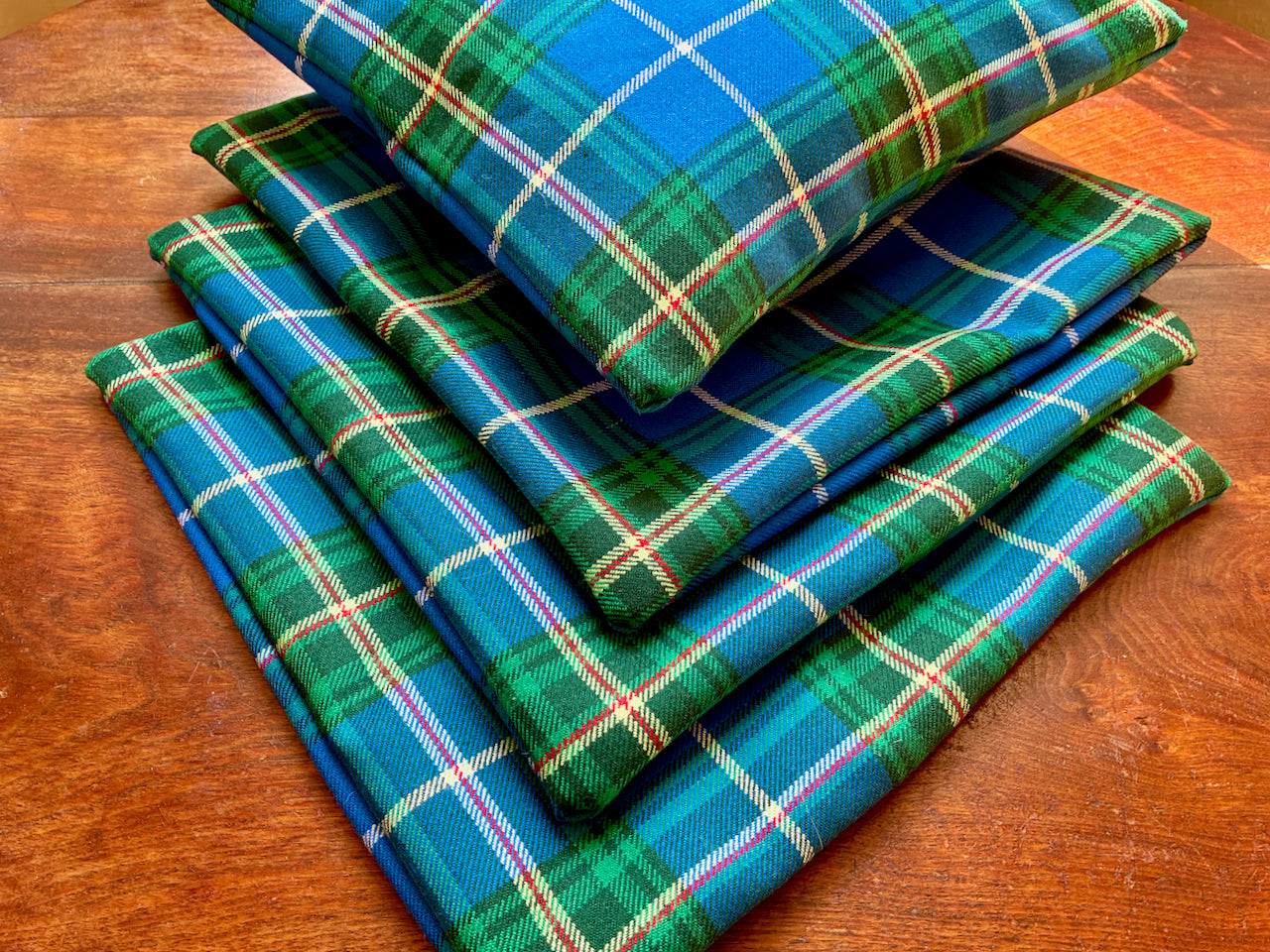 Four Striking  Blue and Green Tartan Cushion Covers, one full, on a wooden surface