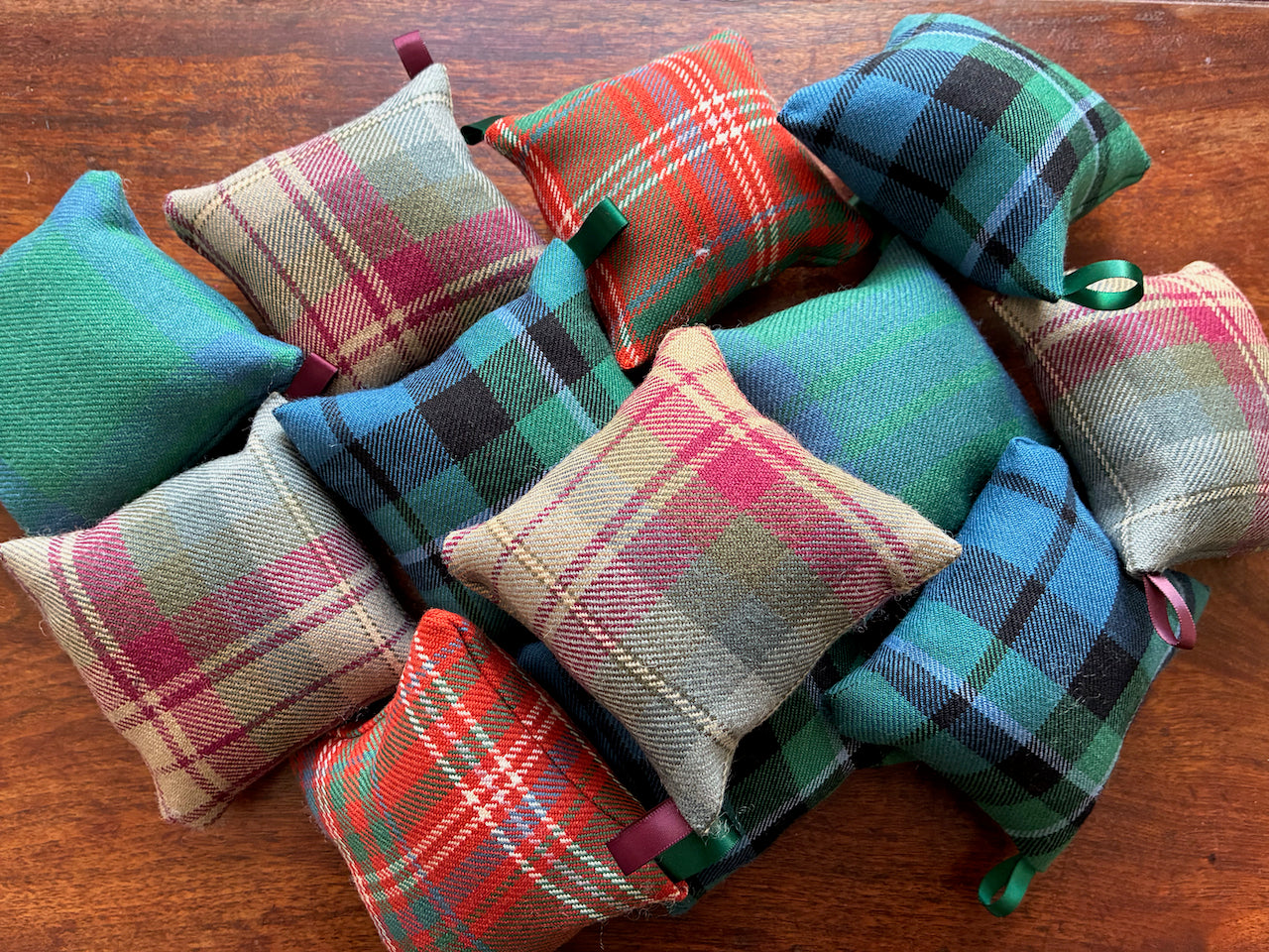 Collection of colourful Tartan Pincushions with Satin hooks on a wooden surface.