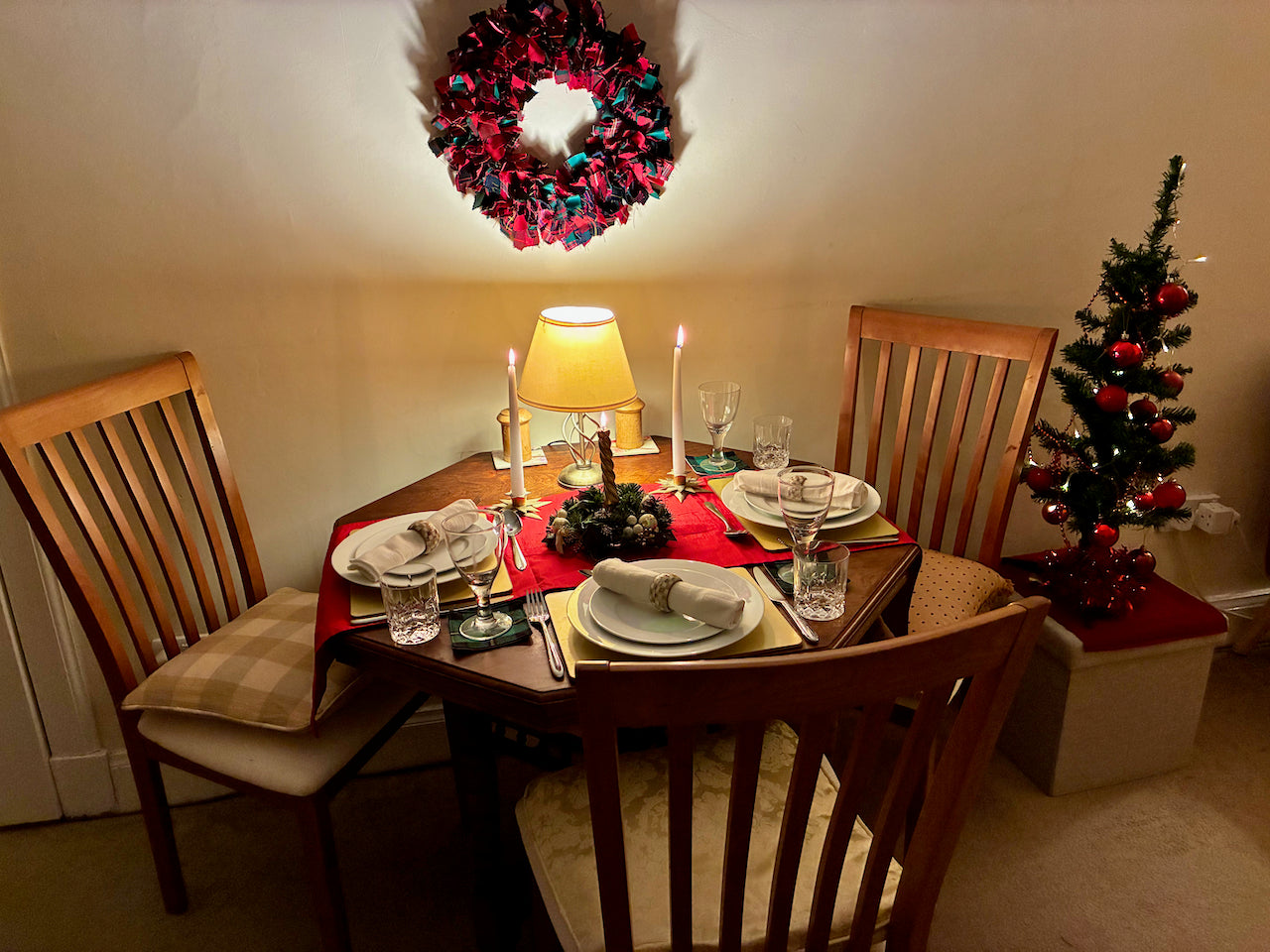 Dining room with a set table, Christmas tree, and wreath on a wall.