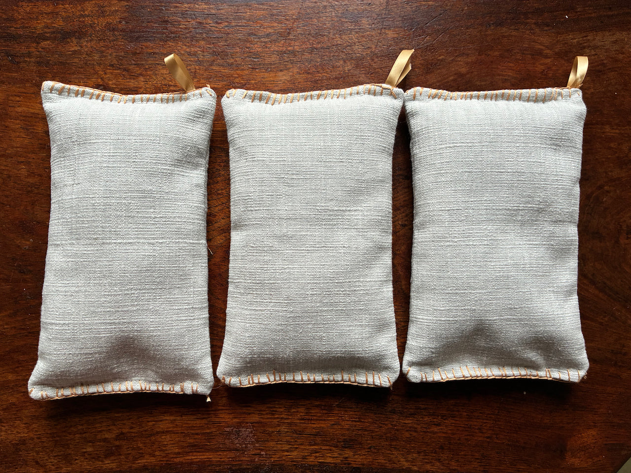 Three Small Linen Wheat Bags with Gold hooks on a wooden surface