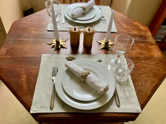 Dining table set with lined Natural Linen Place Mats, plates, cutlery napkins and glasses on a wooden table.