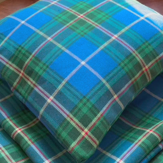 Four square Green and Blue Tartan Cushion Covers, one full, on a wooden surface