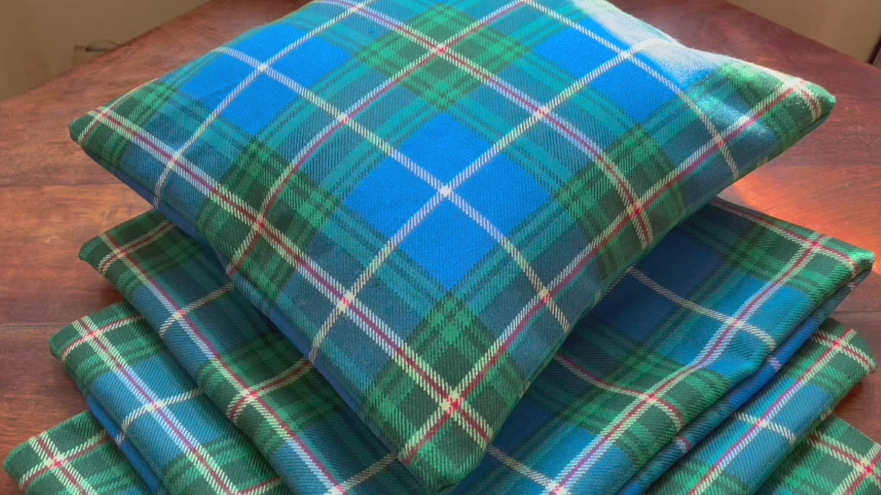 Four square Green and Blue Tartan Cushion Covers, one full, on a wooden surface