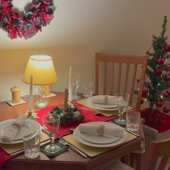 Circular Tartan wreath in reds, greens and golds behind a festive dining table and a lit Christmas tree