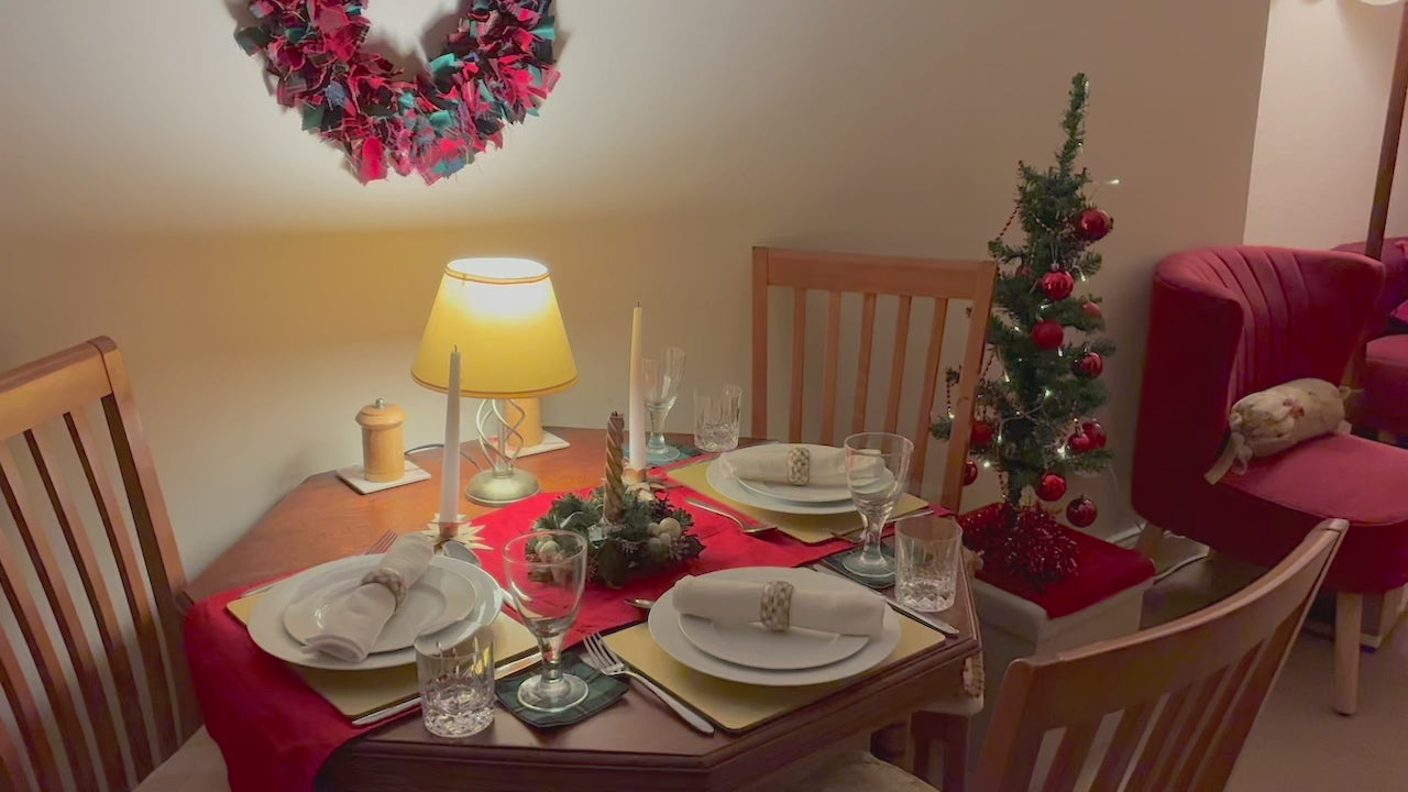 Circular Tartan wreath in reds, greens and golds behind a festive dining table and a lit Christmas tree