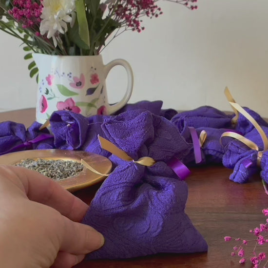 One Purple Lavender Sachet with a saucer of Dried Lavender and a vase of Pink flowers
