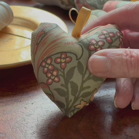 Compact William Morris Heart Pincushion by a saucer with cream thread n it