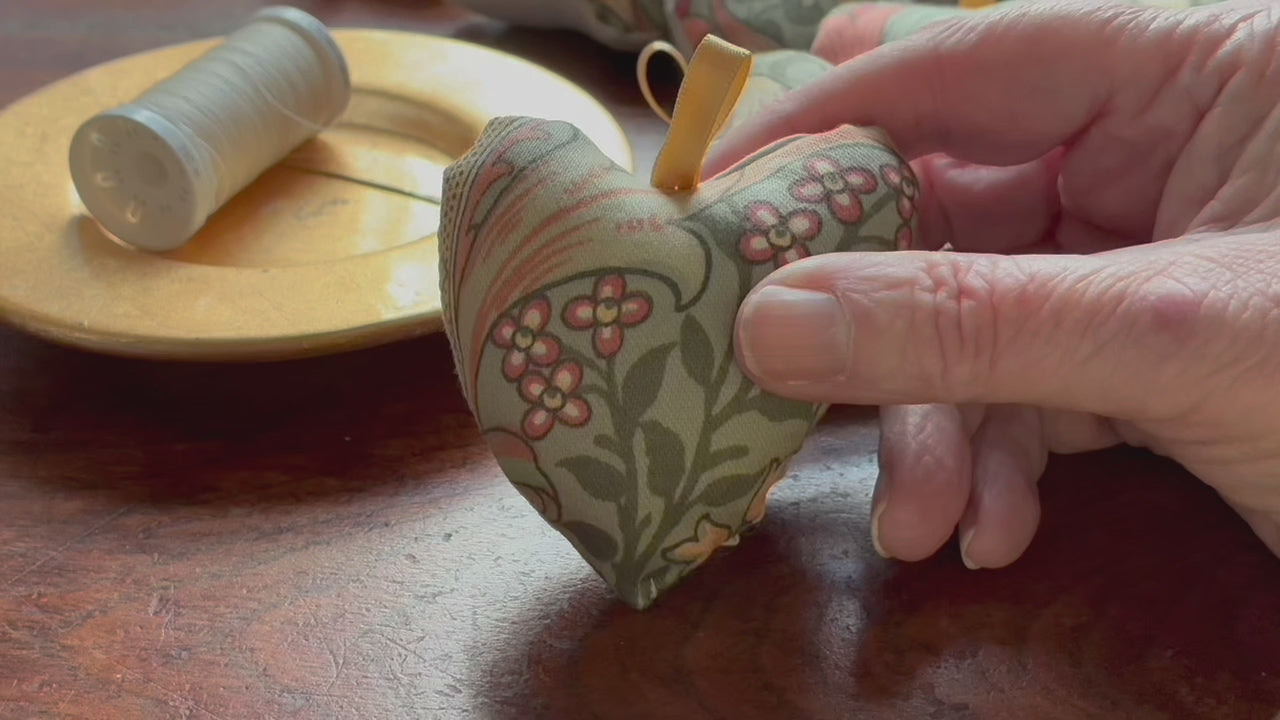 Compact William Morris Heart Pincushion by a saucer with cream thread n it