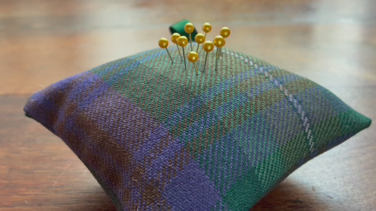 A Tartan Pincushion with Gold pins in it on a wooden surface