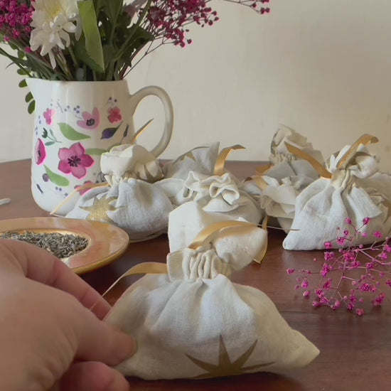 One Cream and Gold Starry Lavender Sachet by a saucer of Dried Lavender and a vase of Pink flowers